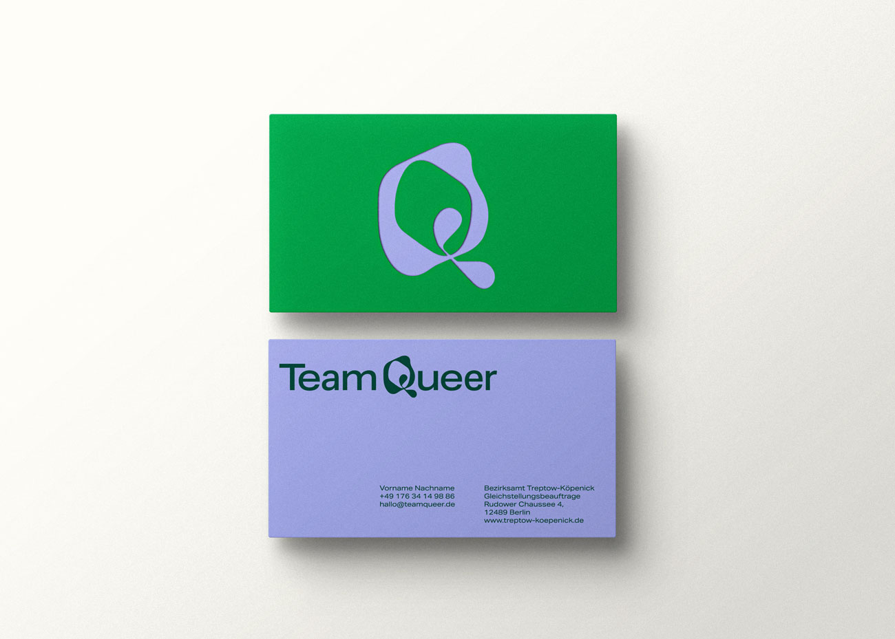 Zwei Visitenkarten liegen übereinander. Auf der oberen, grünen Visitenkarte ist das abstrakte, grafische Q als Bildmarke in violet abgebildet. Die untere Karte ist violet mit dunkelgrüner Schrift. Oben Links das Logo „Team Queer“, darunter in kleiner Schrift die Kontaktdaten.