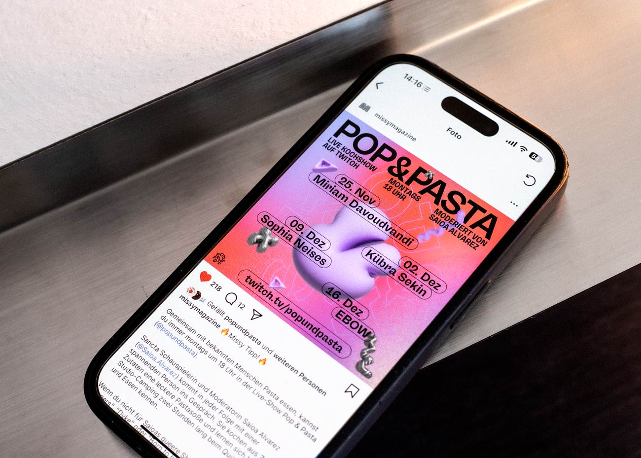 Ein Smartphone liegt auf silbernem Grund. Im Display ist ein Instagrampost des Missy-Magazins geöffnet. Der Post zeigt ein Lila-rot-pinkes Bild. In schwarzer Schrift steht oben Pop & Pasta, mittig im Bild ist ein Fliederfarbenes 3D-Symbol. Daneben und darüber schwarzer Text sowei weitere, kleinere 3D-Symbole in Lila und Silber.