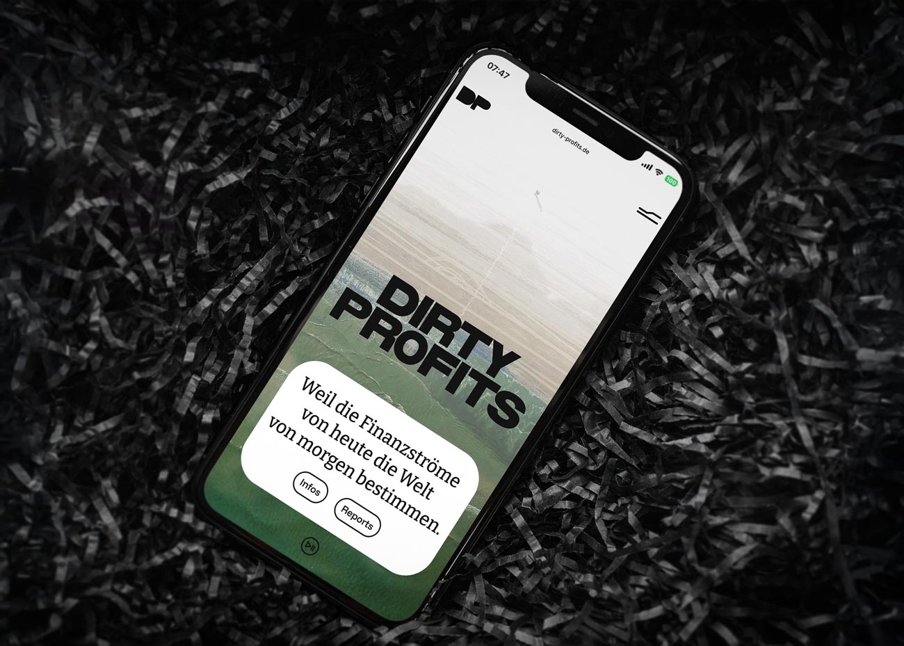 Ein Smartphone liegt auf dunklem geschredderten Papier. Im Display der Header der DirtyProfits-Website. Zentral ist die große Wortmarke auf einem grünlichen Hintergrundbild. Darunter auf einem weißen Kasten der Slogan Weil die Finanzströme von heute die Welt von morgen bestimmen sowie Buttons.