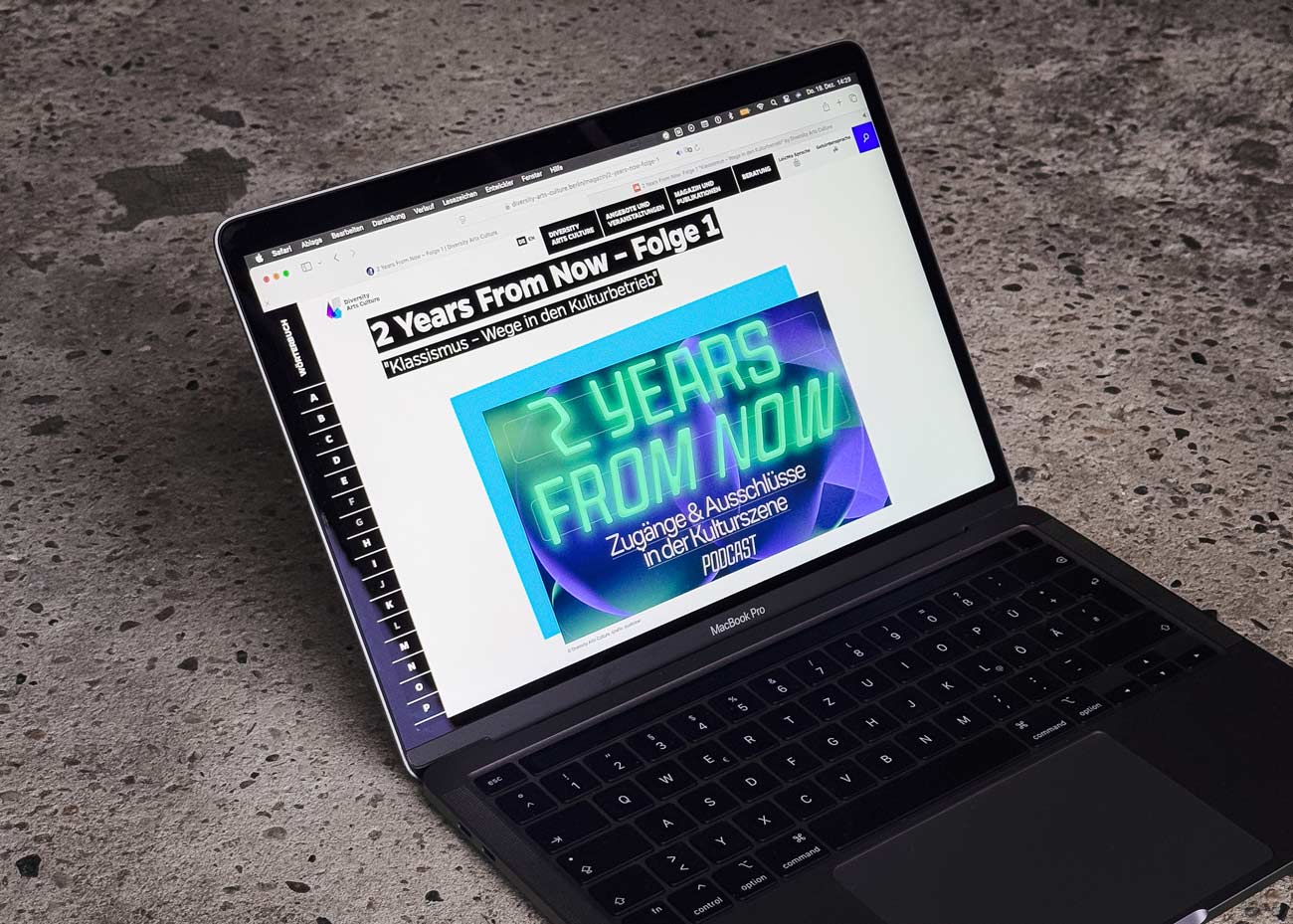 Ein Laptop steht auf einem Beton-Untergrund. Im Monitor die Website von Diversity Arts Culture. Das Podcast-Cover sowie der Titel sind erkennbar.