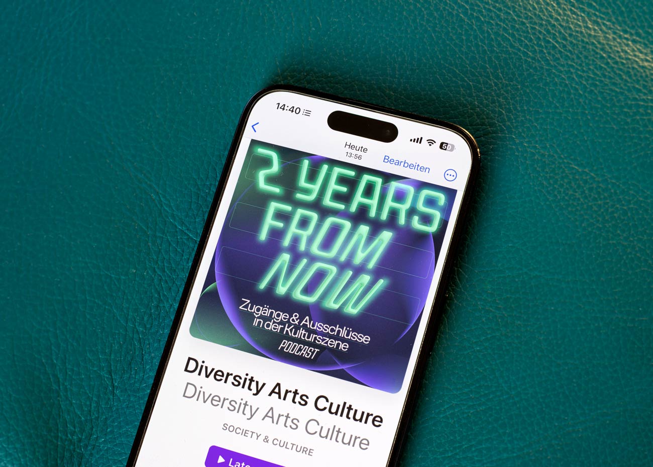 Ein Smartphone liegt auf einem smaragd-grünen, an Leder erinnernden Untergrund. Darauf liegt ein smartphone. Im Display das Podcast-Cover, darunter steht Diversity Arts Culture.