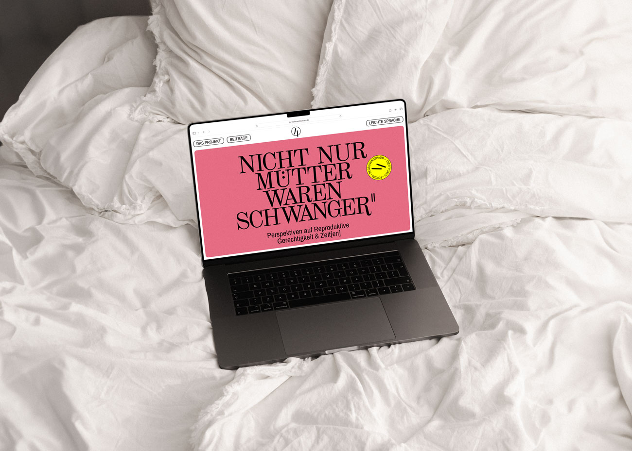 Ein Laptop steht auf einem Bett. Im Display die Startseite von NNMWS2. Auf rosarotem Grund steht der Projekttitel Nicht nur Mütter waren Schwanger, darunter der Slogan Perspektiven auf Gerechtigkeit & Zeit(en).