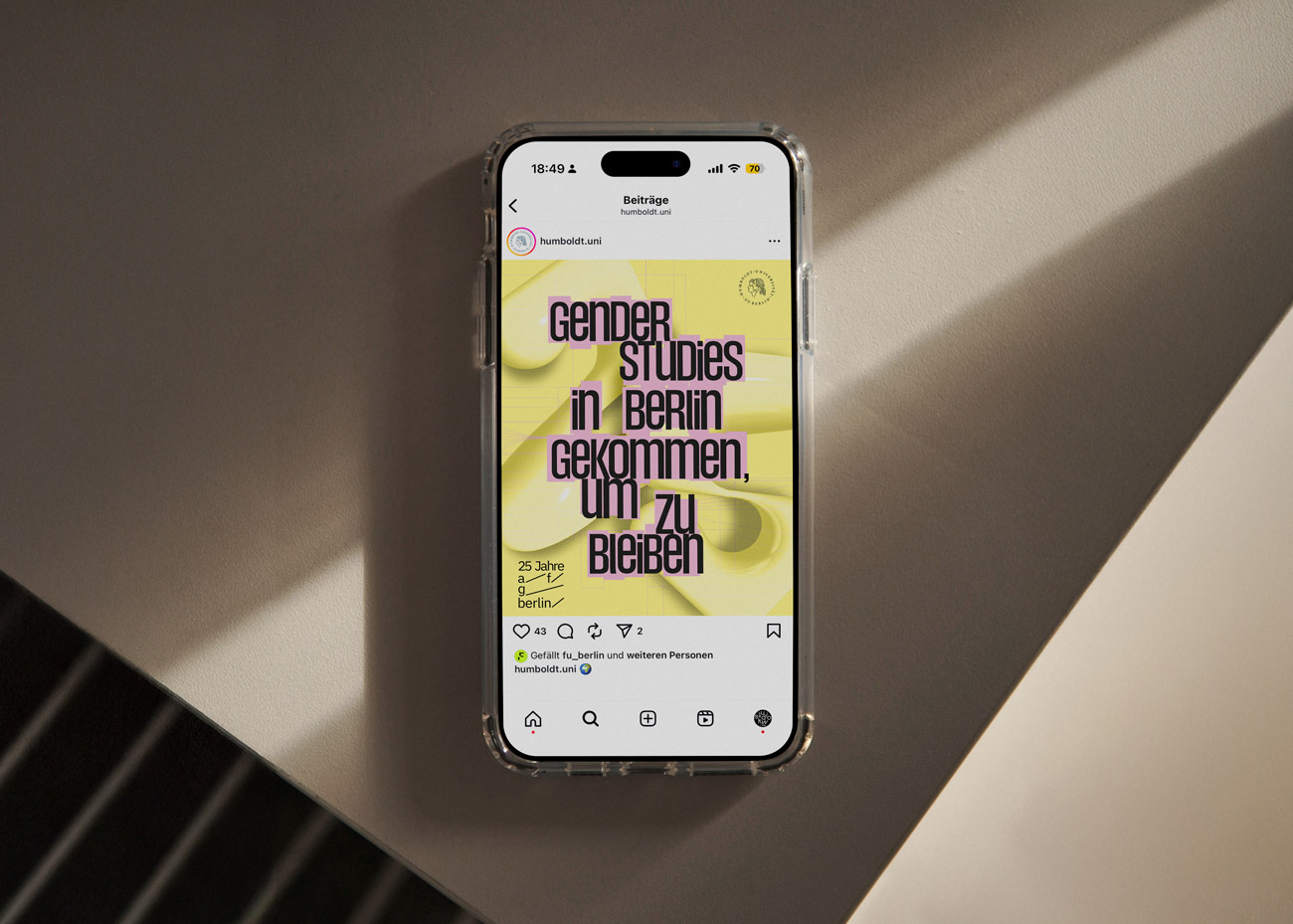 Smartphone mit Instagram-Beitrag, der Text zeigt: 'Gender Studies in Berlin gekommen, um zu bleiben' auf gelbem Hintergrund mit abstrakten Formen.