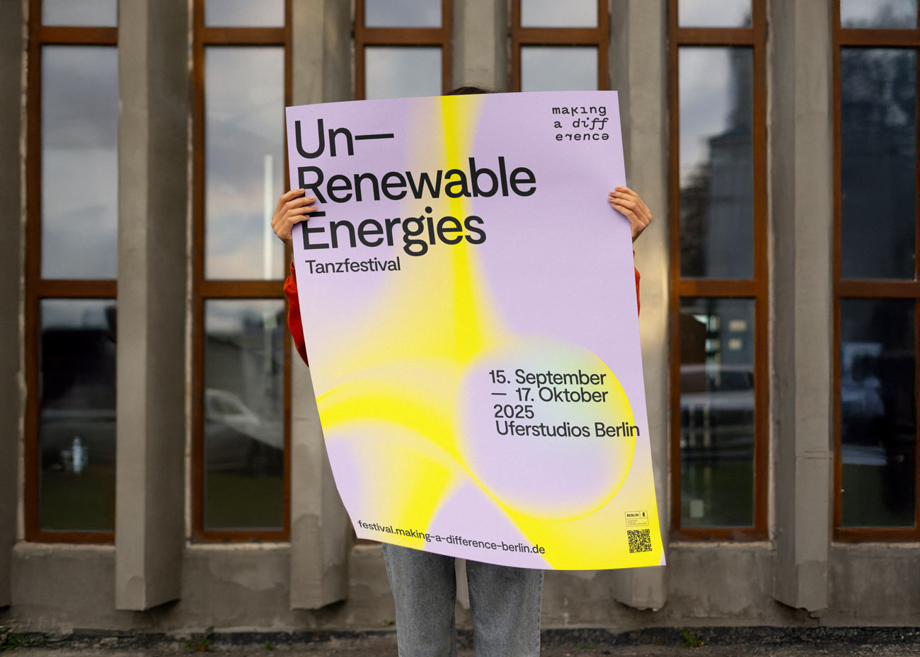 Person hält Plakat mit Text 'Un-Renewable Energies Tanzfestival', Veranstaltungstermine und Ort, gelb-violetter Farbverlauf, vor Fensterfassade