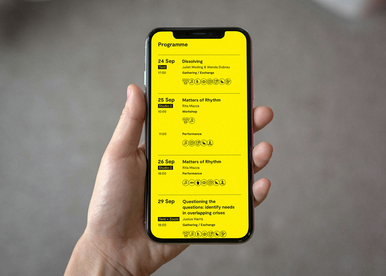 Hand hält Smartphone mit gelbem Bildschirm, darauf Programmübersicht mit Terminen, Uhrzeiten, Titeln, Namen und Symbolen für Veranstaltungen