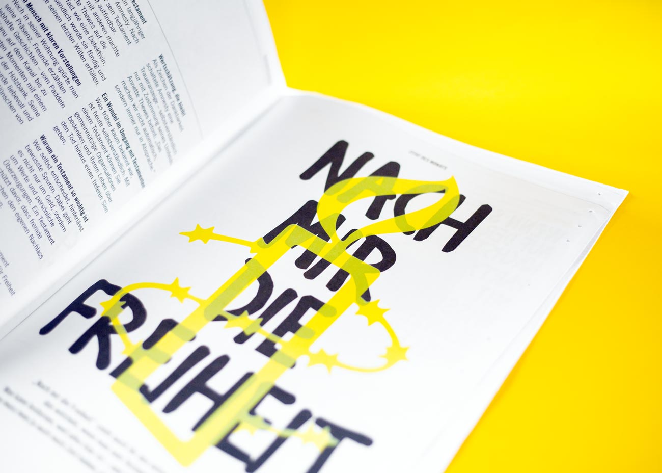 Geöffnete Zeitung auf gelbem Untergrund mit einer Doppelseite, die eine Grafik mit dem Text 'NACH MIR DIE FREIHEIT' zeigt. Der Text ist in großen, schwarzen handgeschriebenen Großbuchstaben gesetzt. Über dem Text liegt eine gelbe Grafik, die eine stilisierte Kerze mit Stacheln darstellt. Die linke Seite der Doppelseite enthält Fließtext in kleinerer Schrift, der in Spalten angeordnet ist.