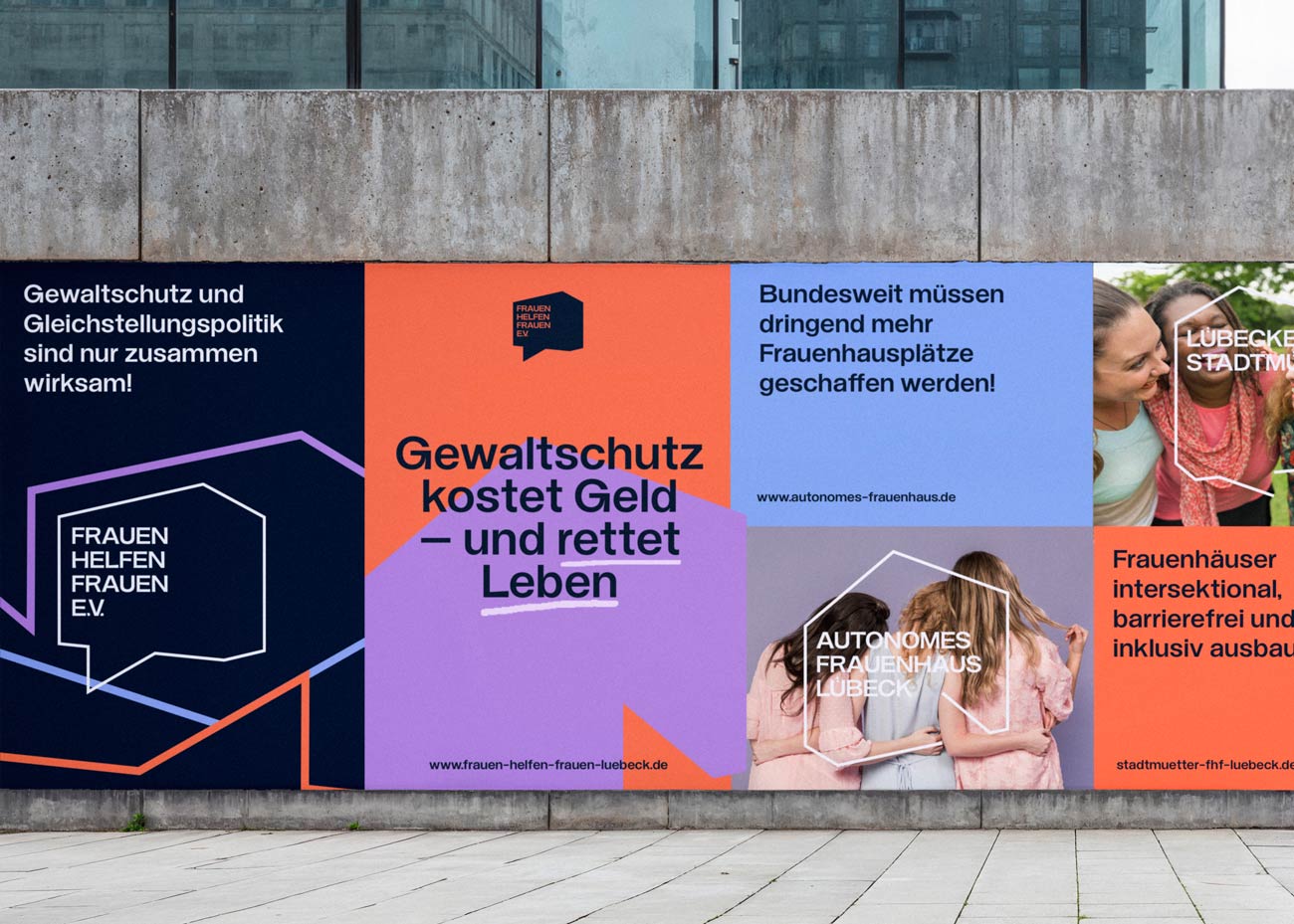 Eine große Plakatwand mit mehreren nebeneinander angeordneten Plakaten. Sie haben unterschiedliche Hintergrundfarben und Texte zur Unterstützung von Frauenhäusern. Das linke Plakat hat einen dunkelblauen Hintergrund mit einem weißen, sechseckigen Rahmen, in dem FRAUEN HELFEN FRAUEN steht, und orangefarbene Linien am unteren Rand. Das mittlere Plakat ist zweigeteilt in Orange und Helllila, mit dem Text Gewaltschutz kostet Geld – und rettet Leben in Schwarz und Orange. Das rechte Plakat hat einen hellblauen Hintergrund mit dem Text Bundesweit müssen dringend mehr Frauenhausplätze geschaffen werden! und darunter ein Foto von zwei Frauen, von denen eine ein weißes T-Shirt trägt, mit dem Logo AUTONOMES FRAUENHAUS LÜBECK in einem weißen sechseckigen Rahmen. Rechts daneben ist ein weiteres Plakat mit orangefarbenem Hintergrund und dem Text Frauenhäuser intersektional, barrierefrei und inklusiv ausbauen. Im Hintergrund ist eine graue Betonwand zu sehen.