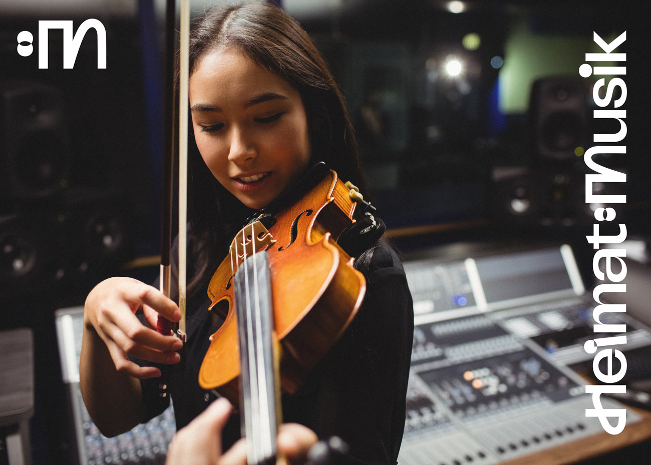 Eine Person spielt in einem Tonstudio Geige. Die Geige ist aus Holz mit vier Saiten und wird mit einem Bogen gestrichen. Im Hintergrund sind ein Mischpult mit zahlreichen Reglern und zwei Lautsprecher zu sehen. Rechts im Bild ist in weißer Schrift senkrecht das Logo 'Heimat:Musik'. Oben links befindet sich das weiße Bildzeichen, das aus einem Doppelpunkt und dem Buchstaben ‚M‘ — aus einem eckigen und einem geschwungen Teil — besteht.