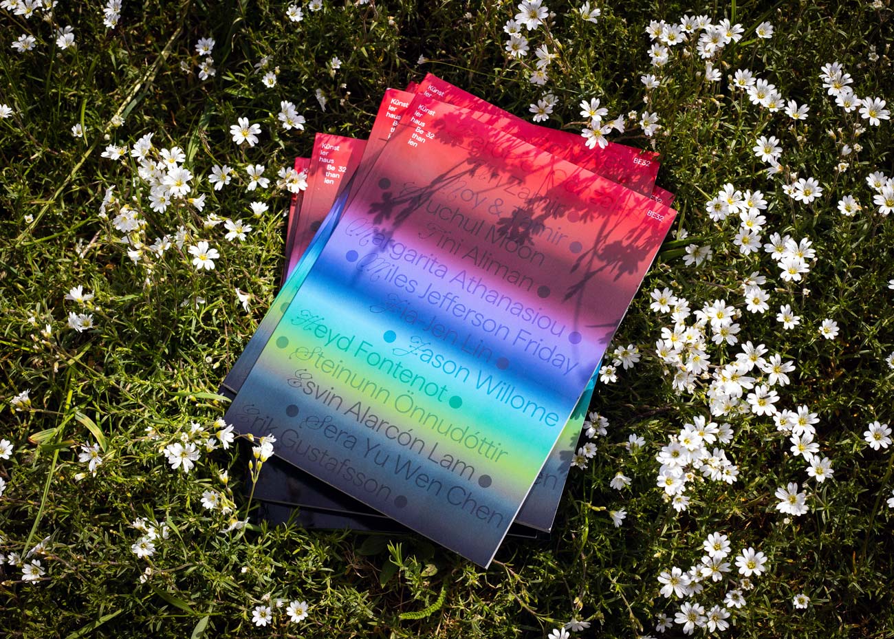Mehrere Ausgaben des Magazins liegen auf einer Wiese mit kleinen weißen Blüten. Das Magazincover zeigen einen Farbverlauf von Rot über Blau zu Grün und ist mit halbtransparenter Schrift bedruckt. Im oberen Bereich ist der Schriftzug »Künstlerhaus Bethanien« zu erkennen.