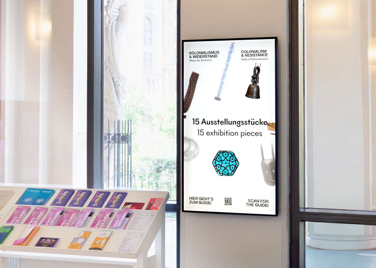 Digitales Informationsdisplay im Eingangsbereich des Museums mit gestaltetem Trailer zur Ausstellung „Kolonialismus & Widerstand“ und QR-Code zum digitalen Guide.