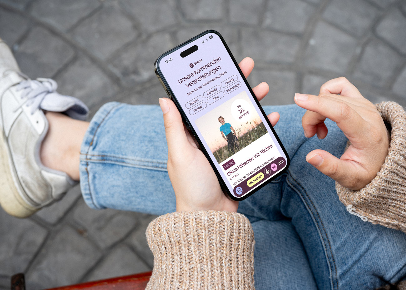 Blick aus der Perspektive einer sitzenden Person auf ein smartphone. Im Display ist die Website des Dachverein Reichenstraße geöffnet und das Design für die Seite Veranstaltungen ist erkennbar.